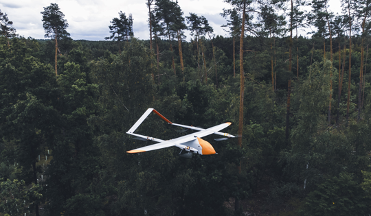 Weiß-orange-farbene Evolonic-Drohne fliegt über Wald um Brände frühzeitig zu erkennen